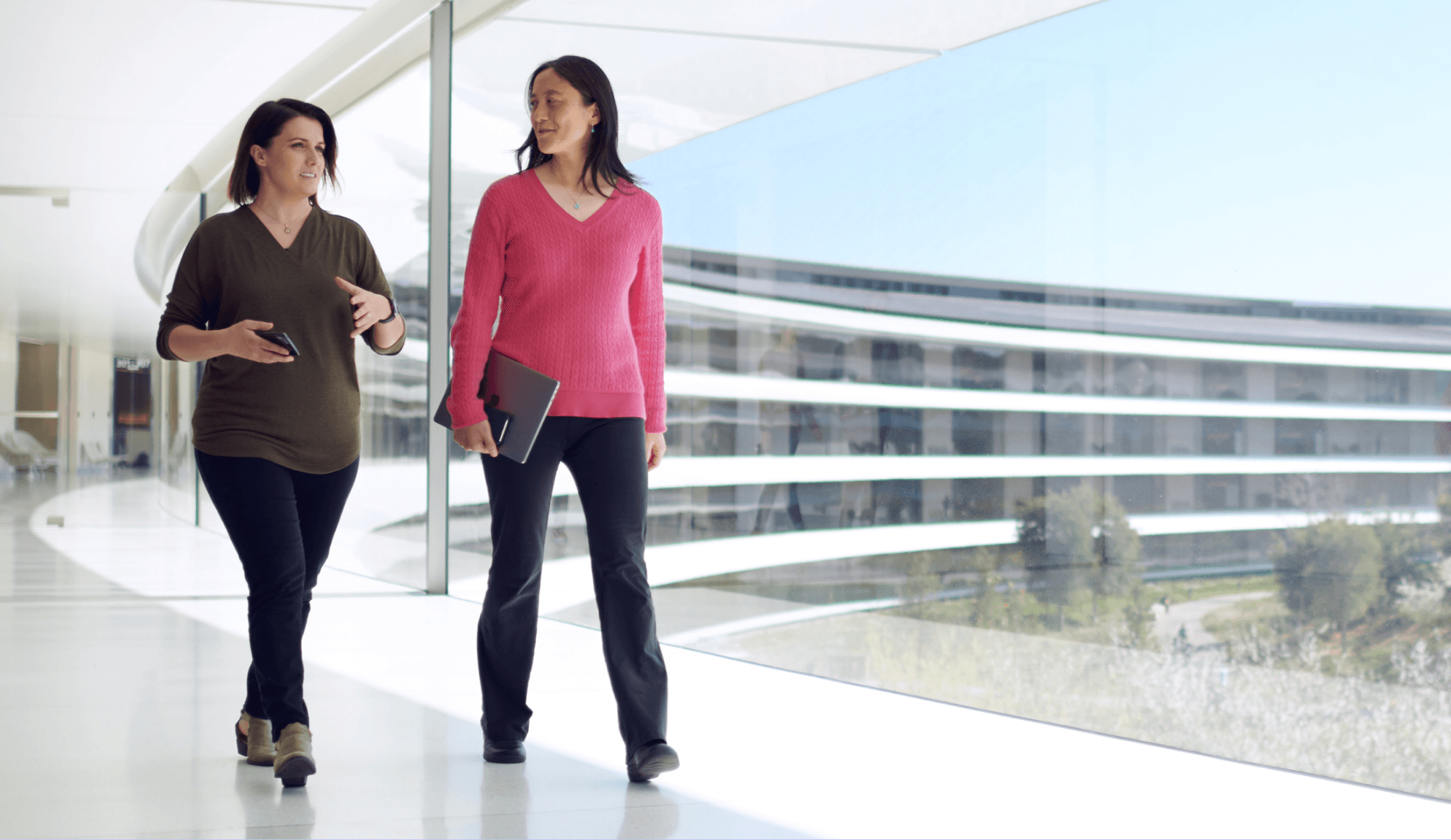 Two people walking through a glass corridor at Apple Park