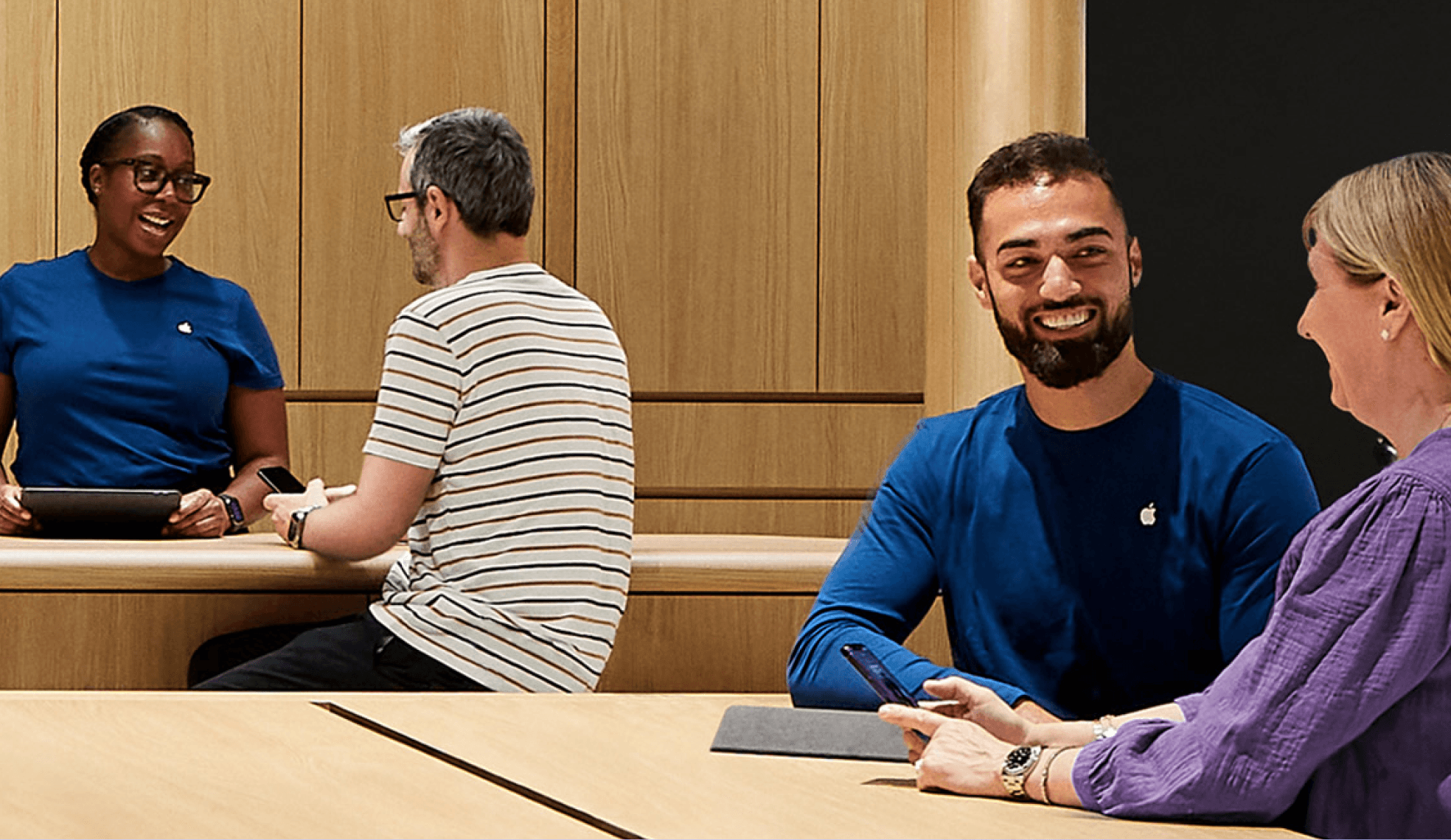 Apple Store employees helping customers at a wooden table